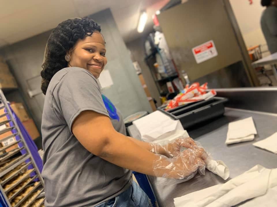 A smiling Refuge volunteer prepares food in a kitchen.